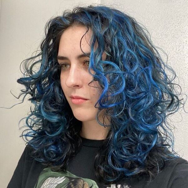 a woman wearing a black printed shirt has a short curly hair with blue highlights