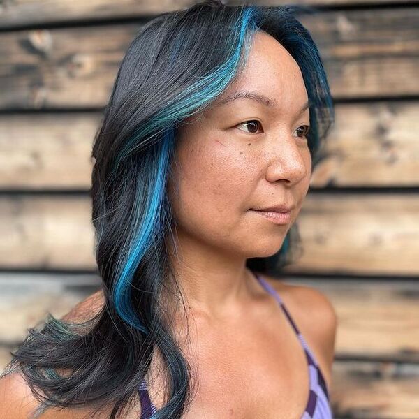 a woman wearing a purple sleeveless top has a blue steaks hairstyle