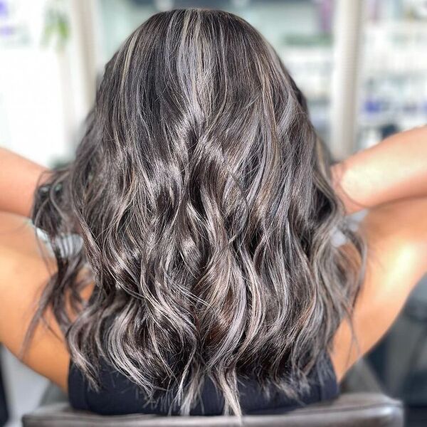 Black Hair with Platinum Streaks - a woman sitting in a salon chair and is holding her hair