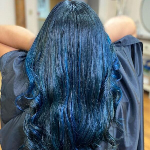 Brilliant Black Blue Hair - a woman holding her hair is wearing a salon cape