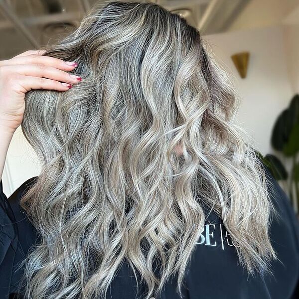 Butter Ash Blonde - a woman wearing a black cape is holding her hair