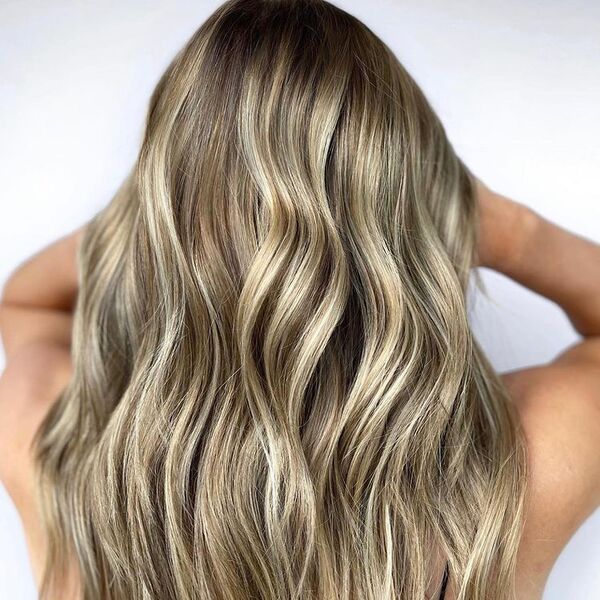 Cinnamon Roll Blonde Balayage - a woman holding her hair up