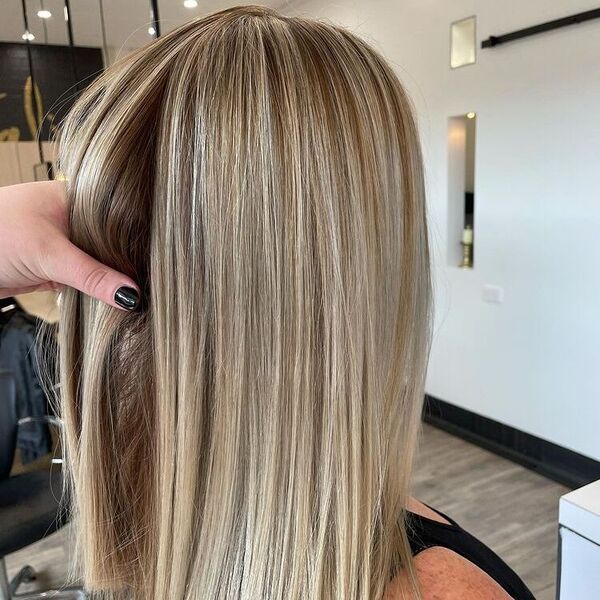 Dimensional Ash Cream Blonde - a woman with a black nail color holding the another woman's hair