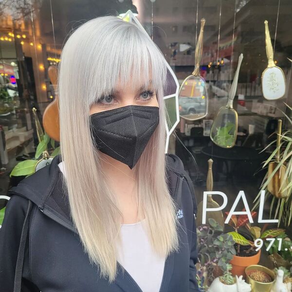 Icy Platinum Blonde with Bangs - a woman wearing a black hooded jacket and a facemask