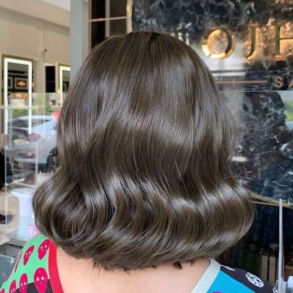 Layered Cut Ash Brown Hair - a woman in a salon wearing a printed shirt