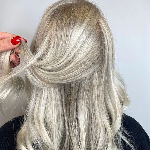 Luxurious Light Ash Brown Blonde - a woman wearing a black shirt and a woman with red nails holding a hair strand