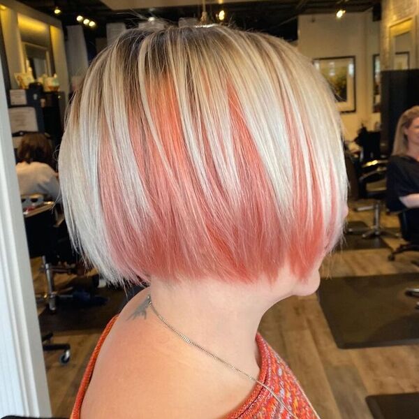 Peachy Keen Platinum Blonde - a woman in a salon wearing an orange knitted top and has a tattoo on her back neck