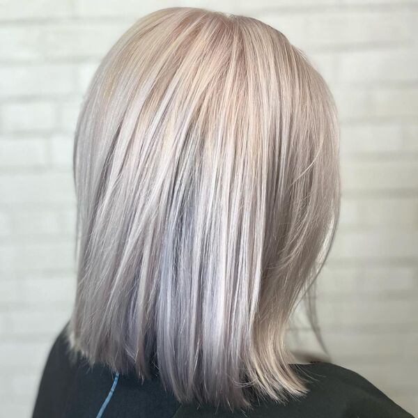 Platinum Blonde with Pearlescent Blue Tint - a woman wearing a black top and is facing a white brick wall