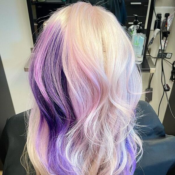 Purple and Pink Tinted Platinum Blonde - a woman sitting in a salon chair and is wearing a black cape