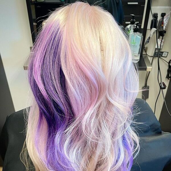 Purple and Pink Tinted Platinum Blonde - a woman sitting in a salon chair and is wearing a black cape