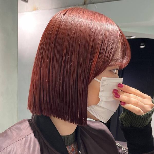 Sleek Straight Red Brown with Fine Bangs - a woman wearing white mask and bummer jacket.