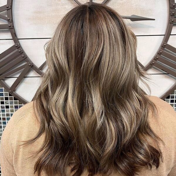 Tone Down Blonde Balayage - a woman facing a large wall clock and is wearing a caramel sweater