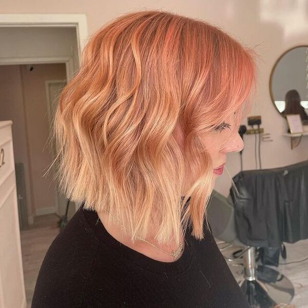 a woman inside a salon having her hair styled to peach rooted hair