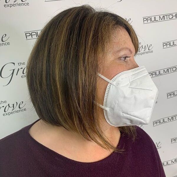 a woman wearing a white KN95 facemask has a graduated bob with caramel highlights