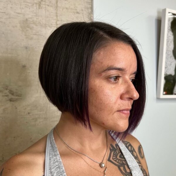 a woman with tattoo wearing a necklace has a asymmetrical graduated bob