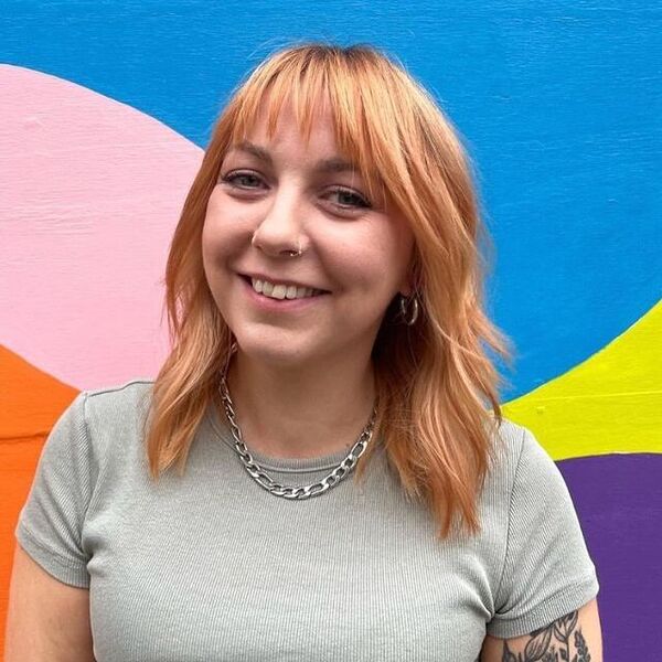 Soft Peach Blonde with Bangs - a woman wearing a gray top